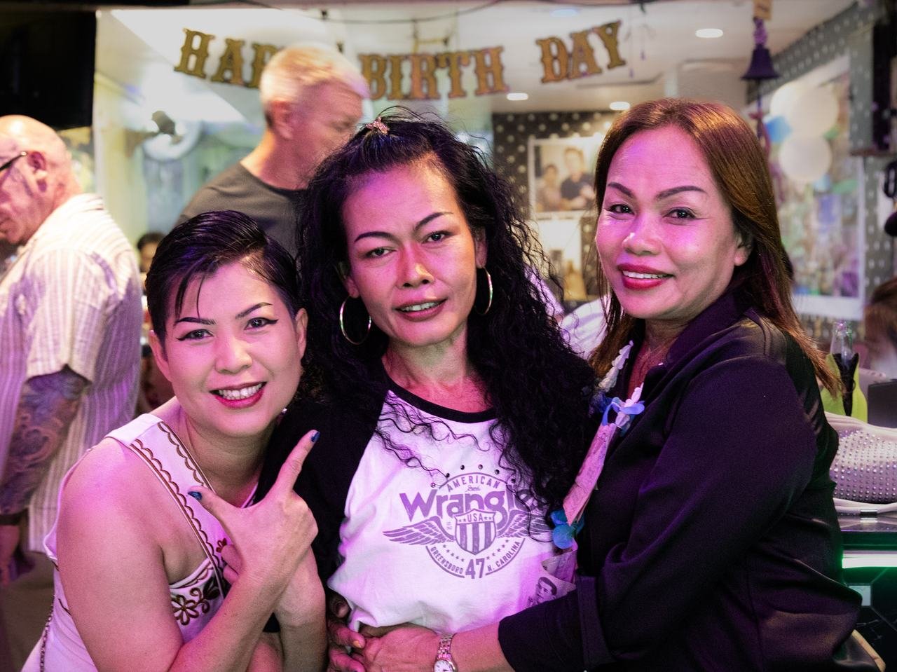 Three friends posing together under the birthday banner
