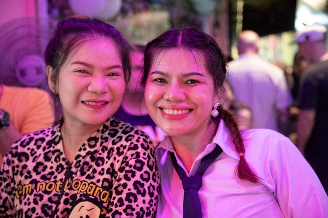 Two friends grinning close together in the neon glow